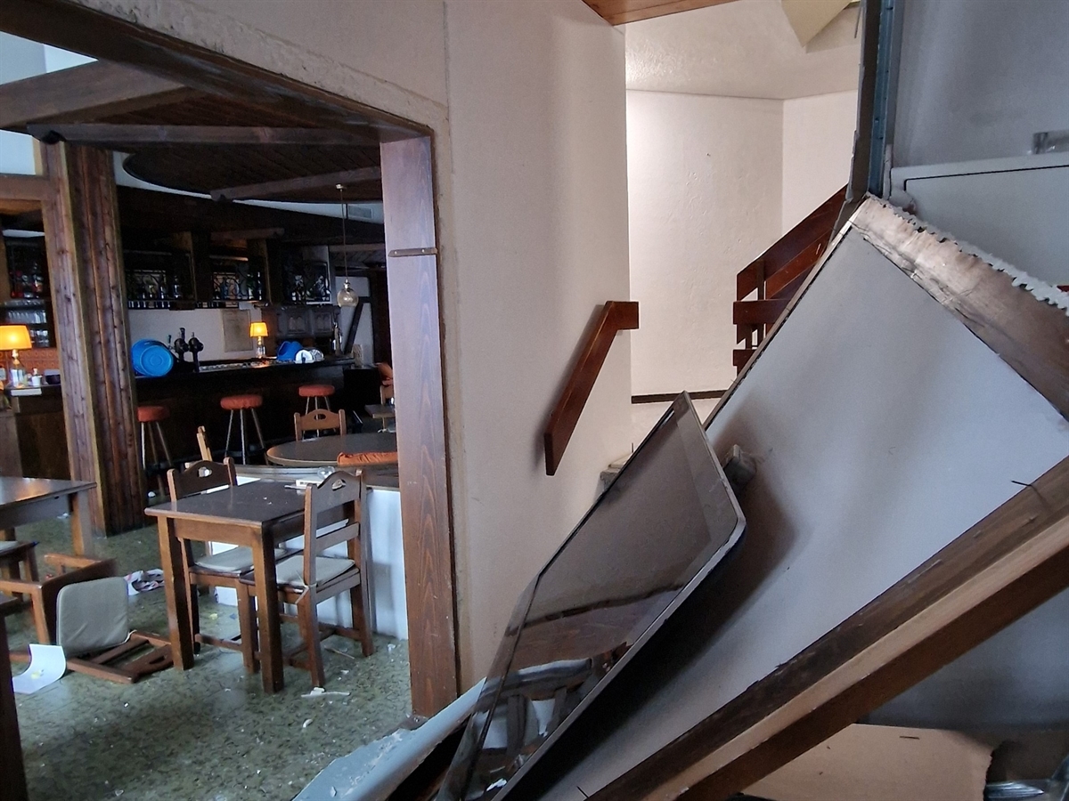 Aufnahme aus dem Treppenhaus in den Innenbereich des Restaurants. Das Mobiliar ist teilweise beschädigt und eine Wand mit Fernseher liegt umgedrückt im Treppenhaus.
