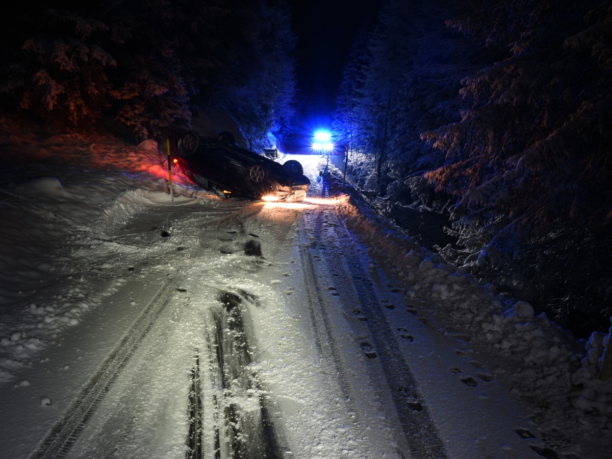 Nachtaufnahme, die schneebedeckte Strasse mit Rutschspuren, welche links an die Böschung gehen. Unmittelbar danach das Auto auf dem Dach. Im Hintergrund Blaulicht eines Polizeiautos.