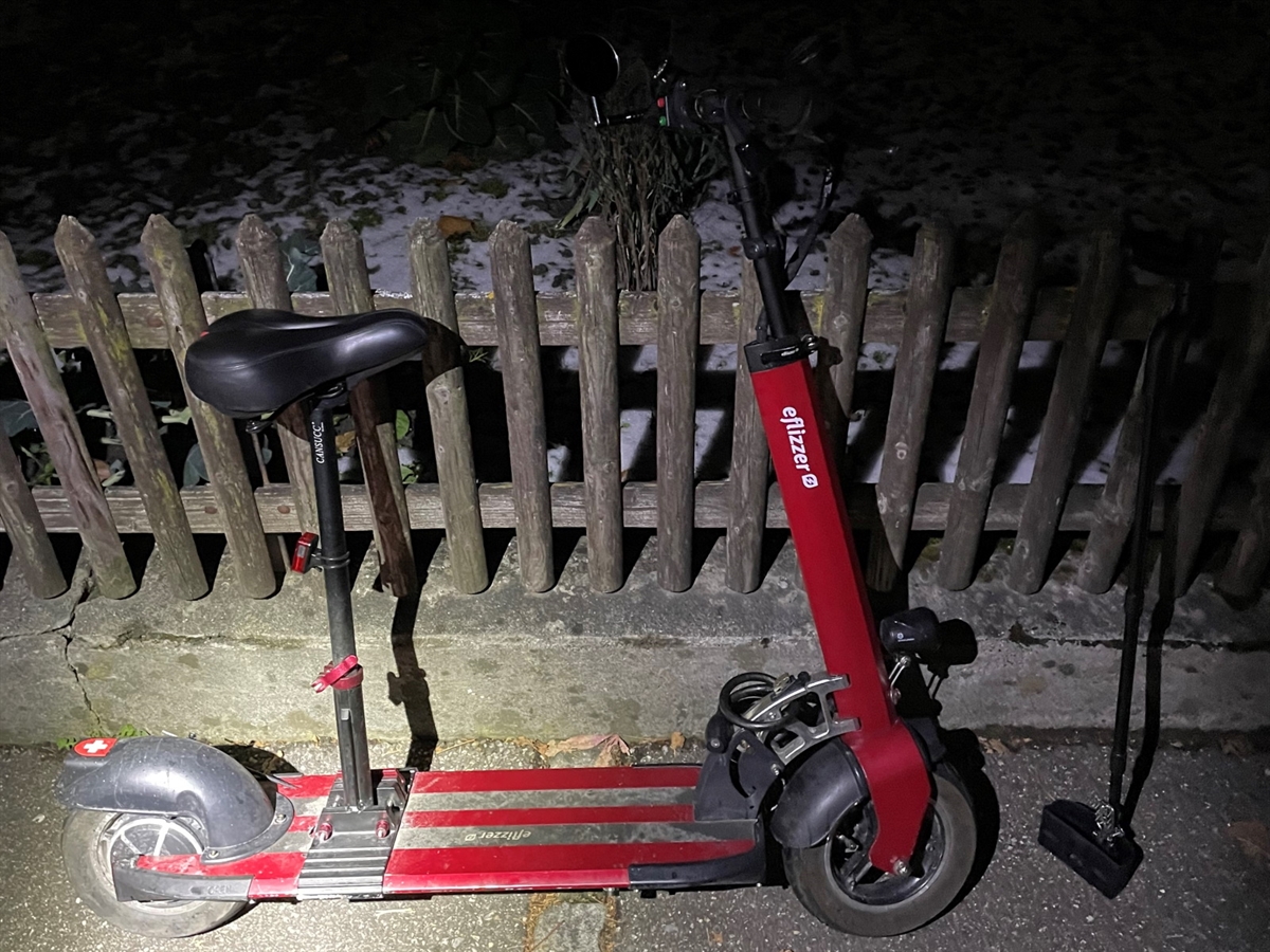 Ein an einen Holzzaun angelehnter roter E-Scooter.
