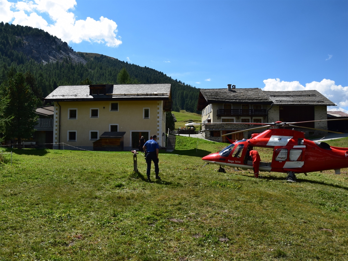 Das Haus im Hintergrund von welchem der Arbeiter herunter fiel. Vorne rechts der Helikopter der Rega sowie ein Polizist der Kantonspolizei Graubünden.