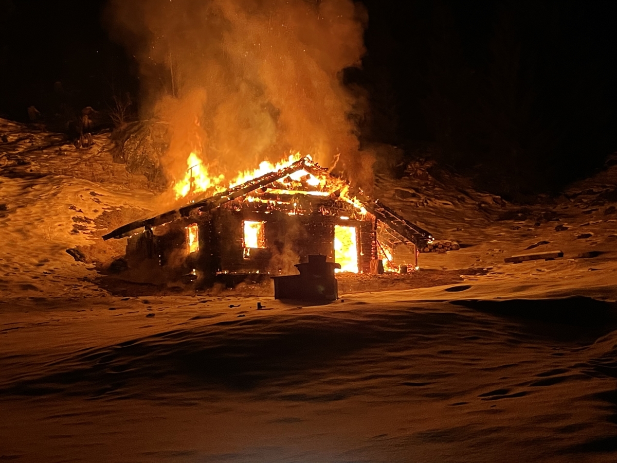 Die brennende Hütte in der Nacht. Das Brandobjekt ist von einer Schneelandschaft umgeben.