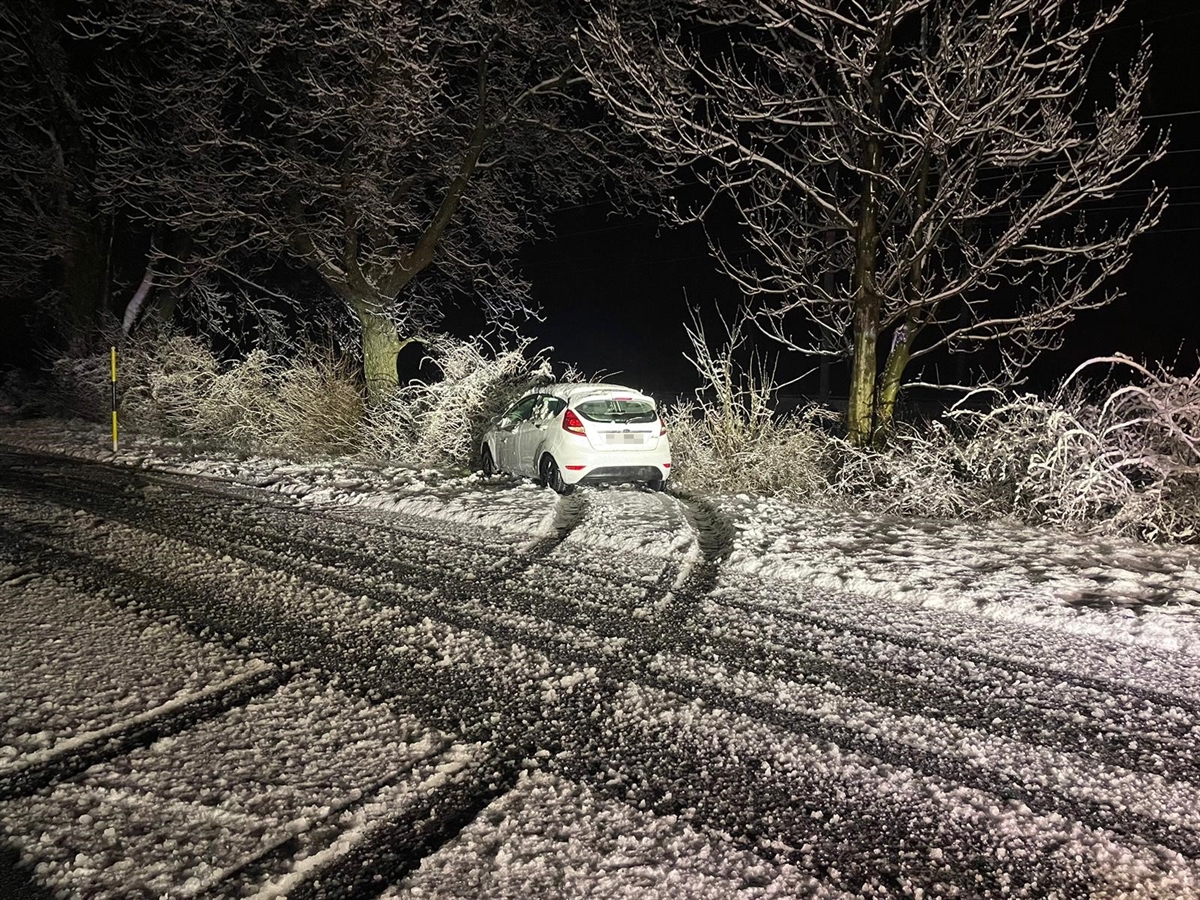 Auf der schneebedeckten Fahrbahn sind die Reifenspuren zu erkennen. Im Hintergrund die Endlage des Fahrzeuges neben der Strasse.