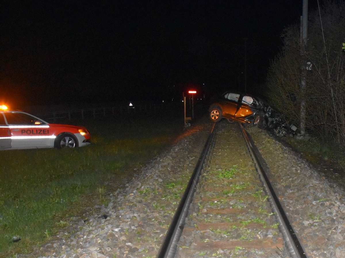 Nachtaufnahme. Links im Wiesland ein Polizeiauto, rechts davon die Gleise der RhB, darauf steht das total beschädigte dunkle Unfallauto.