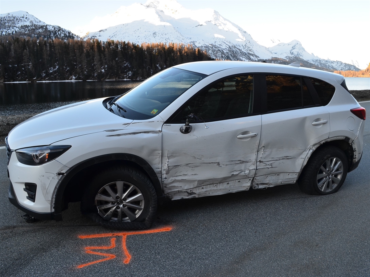 Ein weisser vorne links und seitlich beschädigter SUV. Im Hintergrund der Silsersee und sich vom Horizont abgrenzende Berge. 