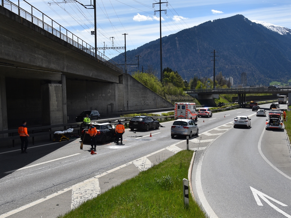Autobahnanschluss Chur Nord. Auf der Überholspur stehen die beiden Unfallfahrzeuge, ein Ambulanzfahrzeug sowie ein Notarztauto. Drei Polizisten und zwei Rettungssanitäter stehen in unmittelbarer Nähe der Unfallfahrzeuge.