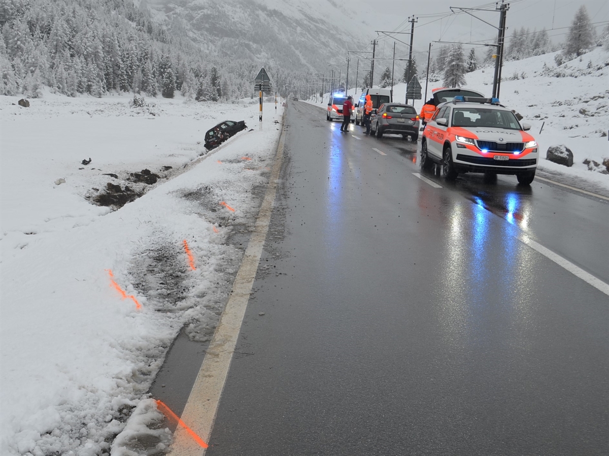 Auf der Strasse zwei Polizeiautos und zwei weitere Autos. Links davon Spuren im Schnee, die zum Unfallauto – es steht beschädigt im Strassenbord – führen.