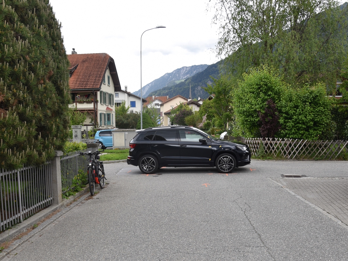 Sicht aus der Perspektive des Radfahrers. Das Unfallauto steht quer in der Verzweigung, respektive versperrt vollständig die Dorfstrasse. Auf der linken Seite ist das E-Bike an einen Zaun angelehnt.