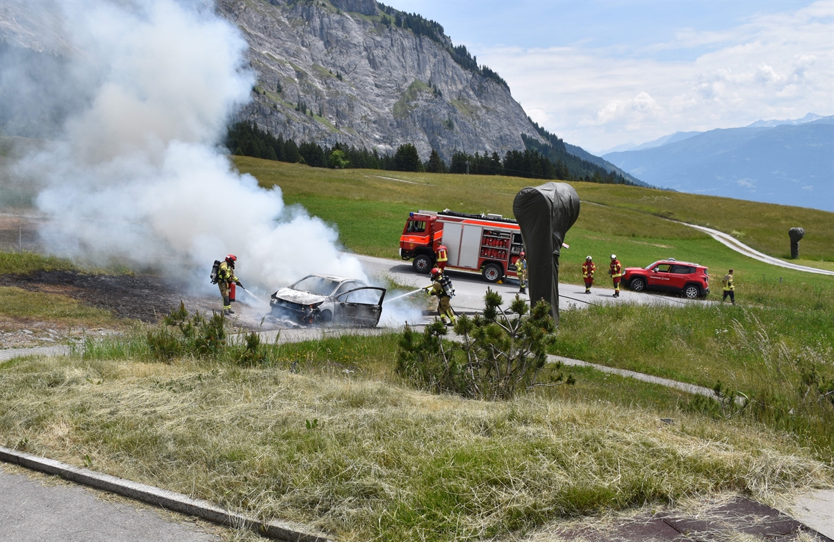 Rauch steigt aus dem Fahrzeug, Feuerwehrleute löschen mit Wasser