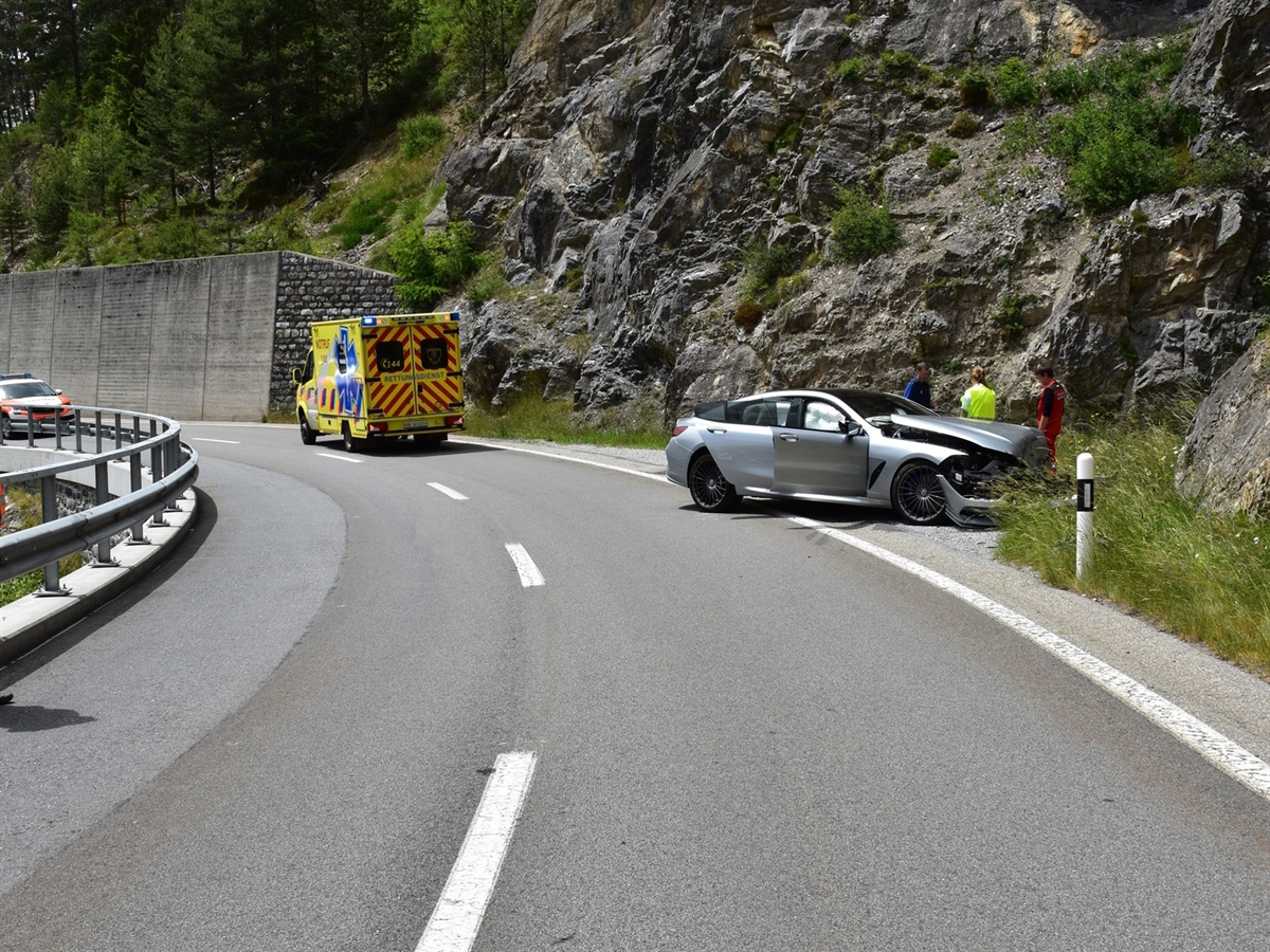 Rechts das Unfallauto nahe der Felswand. Dahinter Einsatzkräfte. Links davon ein Rettungswagen und ein Polizeiauto.