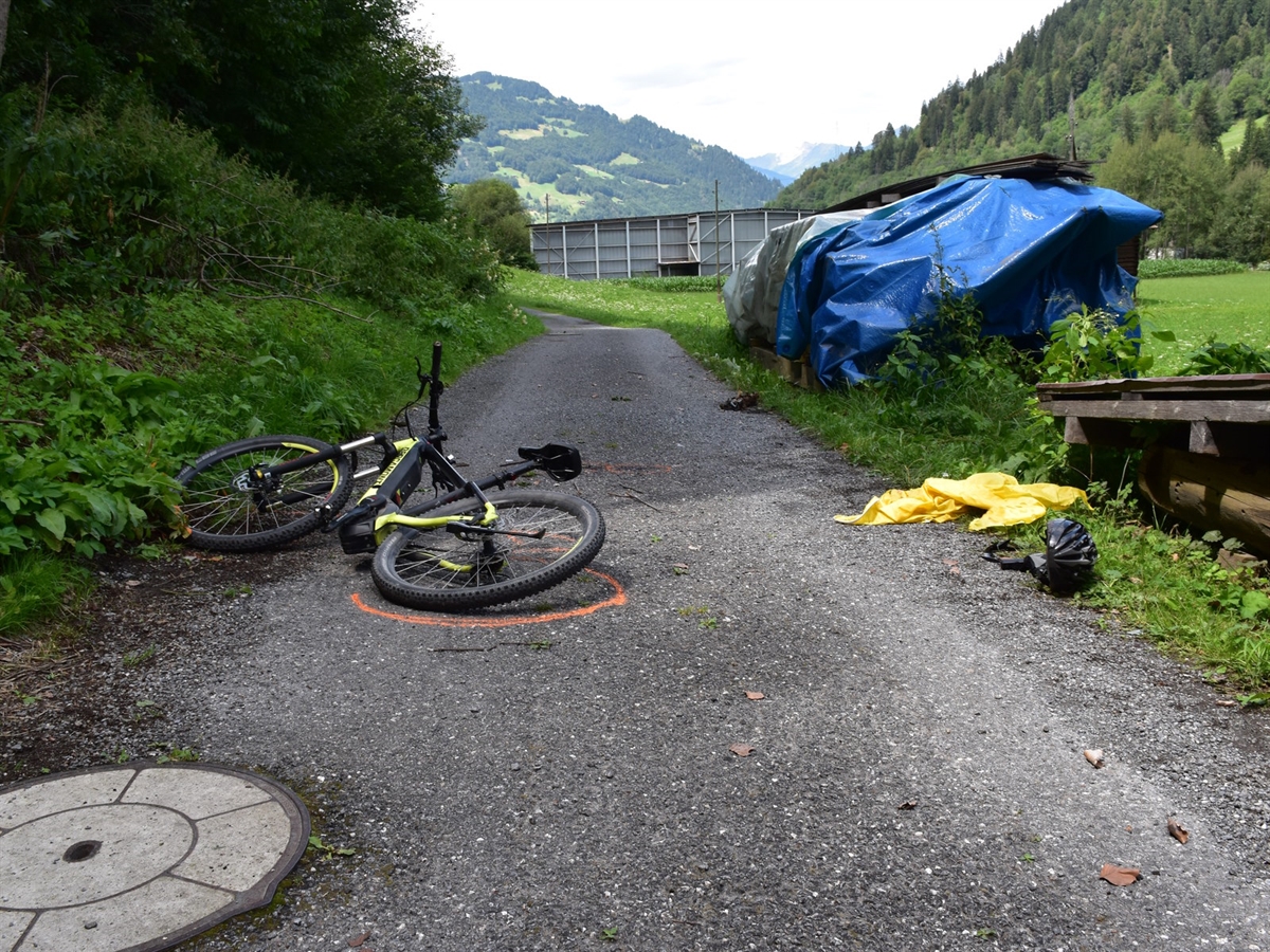 Links ein Waldrand, rechts davon der Feldweg. Auf diesem liegt das Fahrrad, ein Fahrradhelm und eine Jacke. Im Hintergrund der Talboden und der Horizont. 