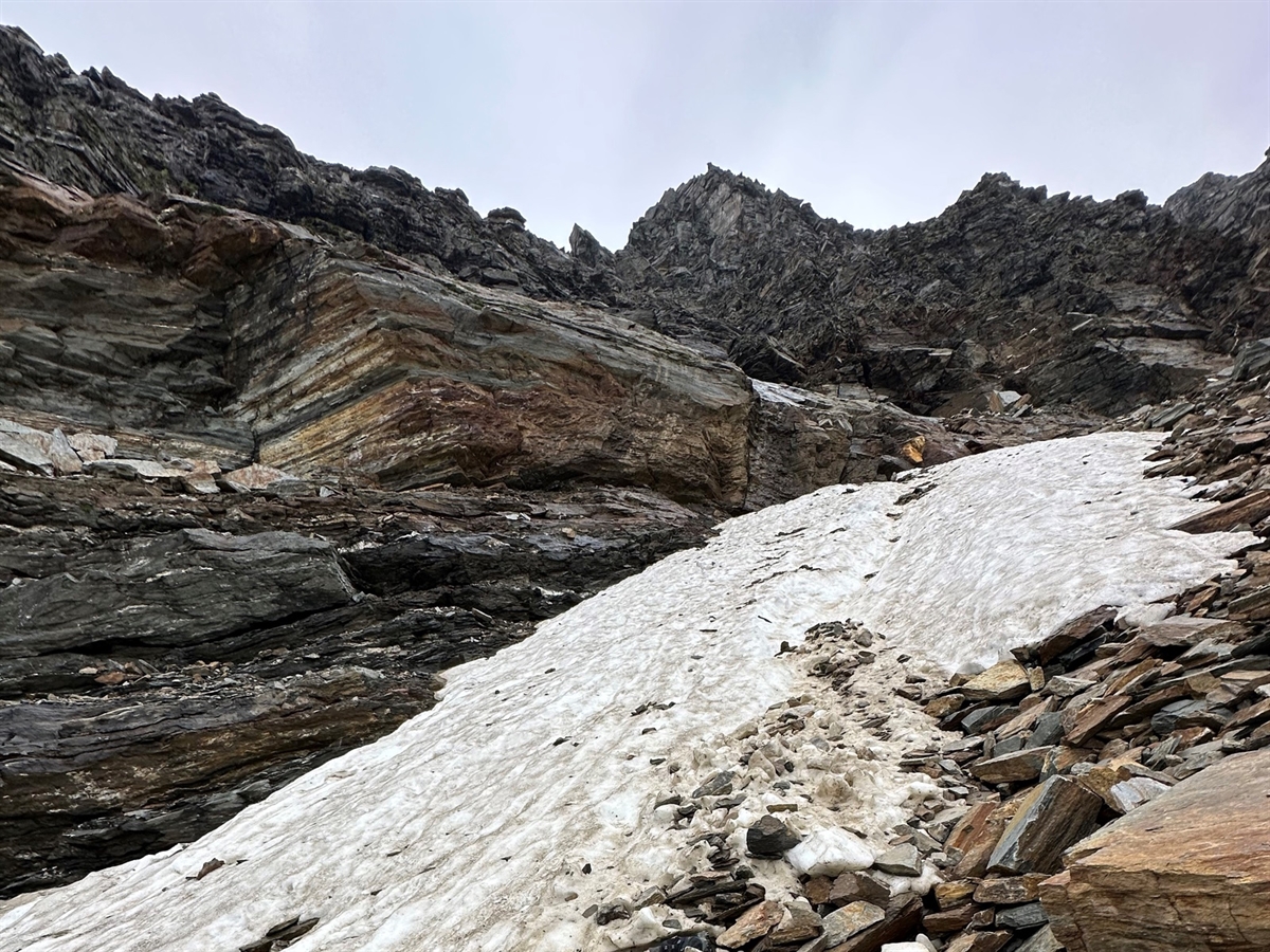 Ein Schneefeld von unten, welches oben von Felsen abgegrenzt wird. Berge grenzen den Horizont ab.