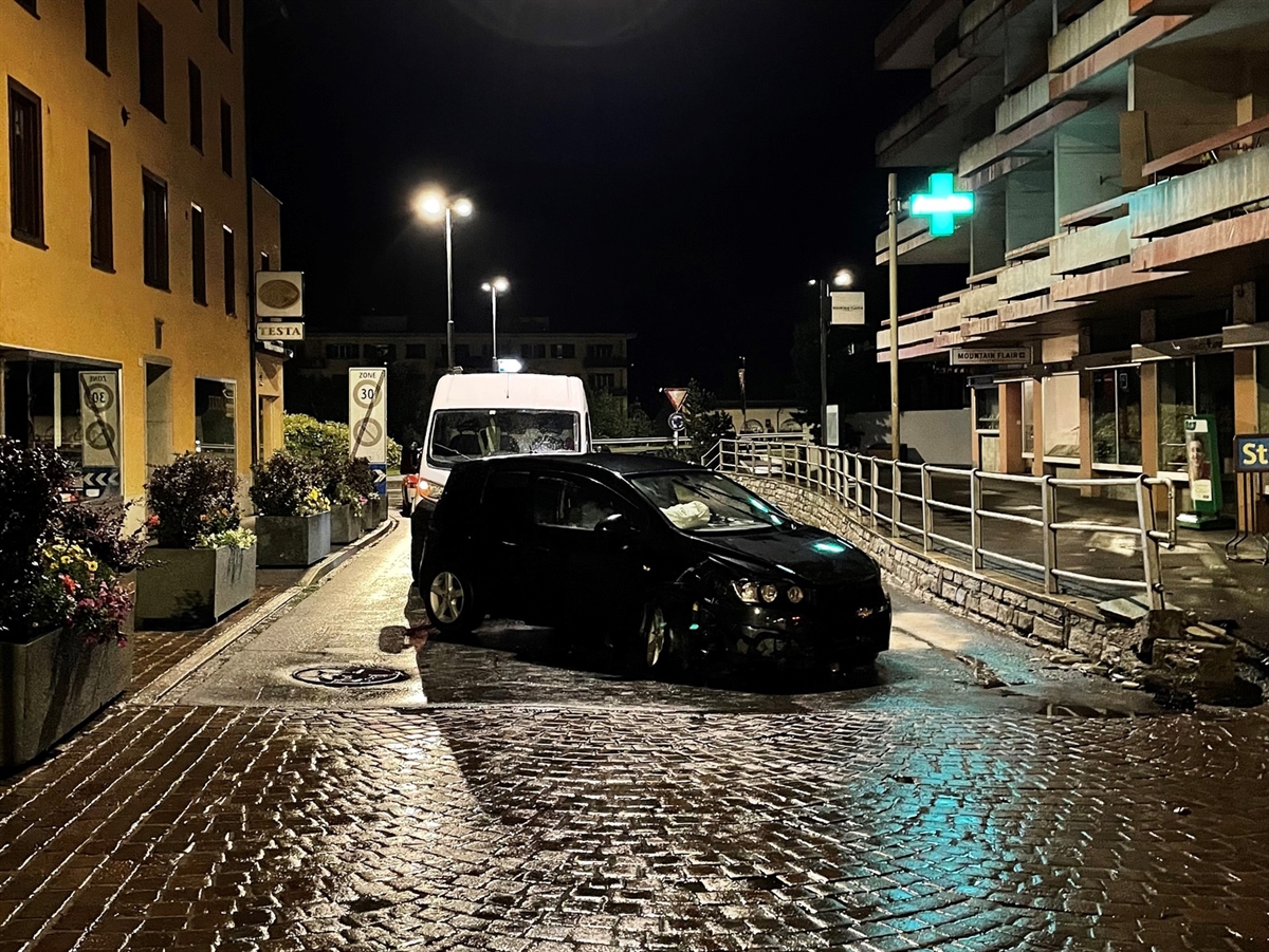 Nachtaufnahme mit schräg auf der Strasse stehendem schwarzen Auto. Links und rechts Gebäude.
