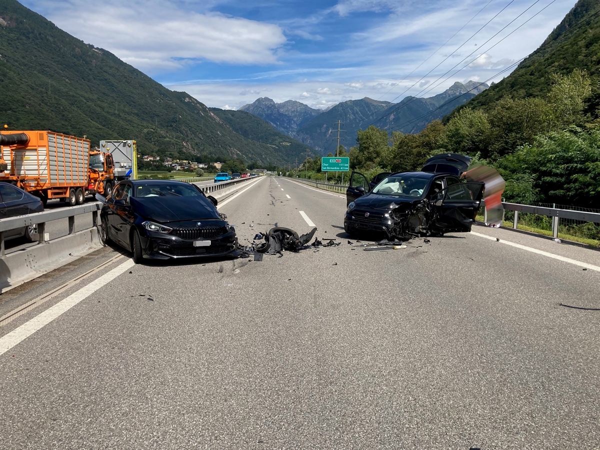 Links und rechts von vorne jeweils ein schräg in die Strassenmitte stehendes schwarzes Auto mit jeweils total beschädigter linker Front. Im Hintergrund Berge und leicht bewölkter Himmel.