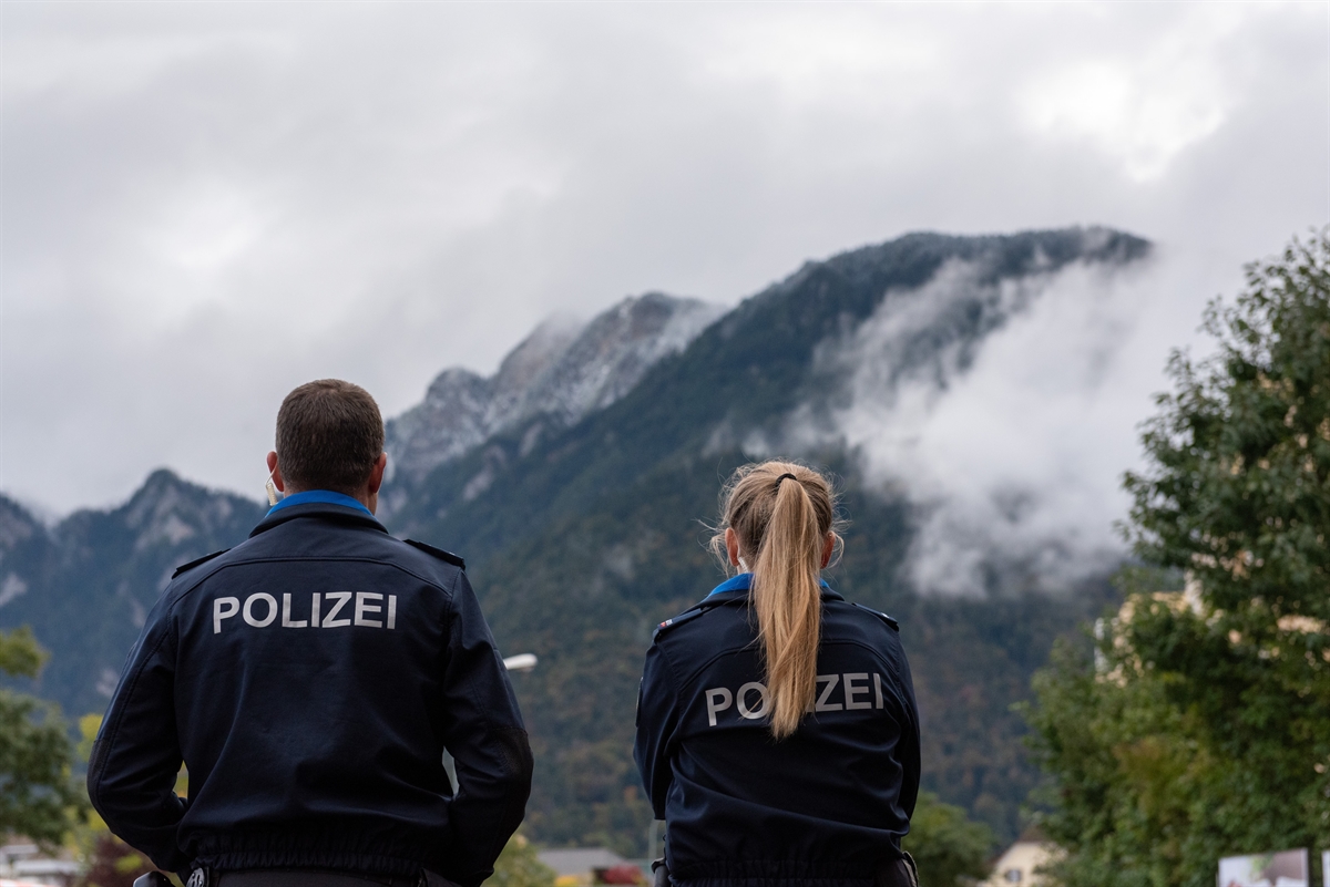 Eine Polizistin und ein Polizist von hinten, schauen die Berge an
