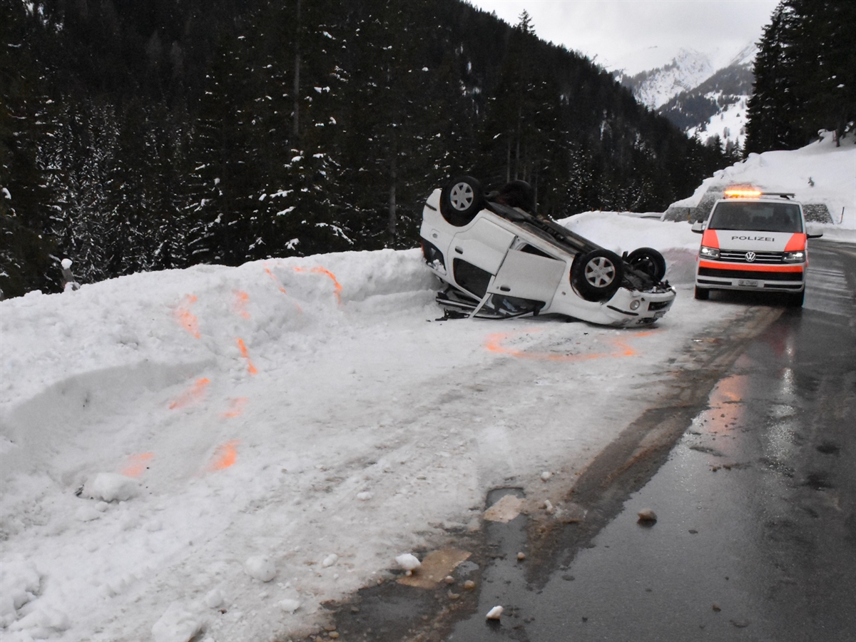 Ein weisser Kleinwagen liegt auf dem Fahrzeugdach. Rechts davon ein Polizeiauto.
