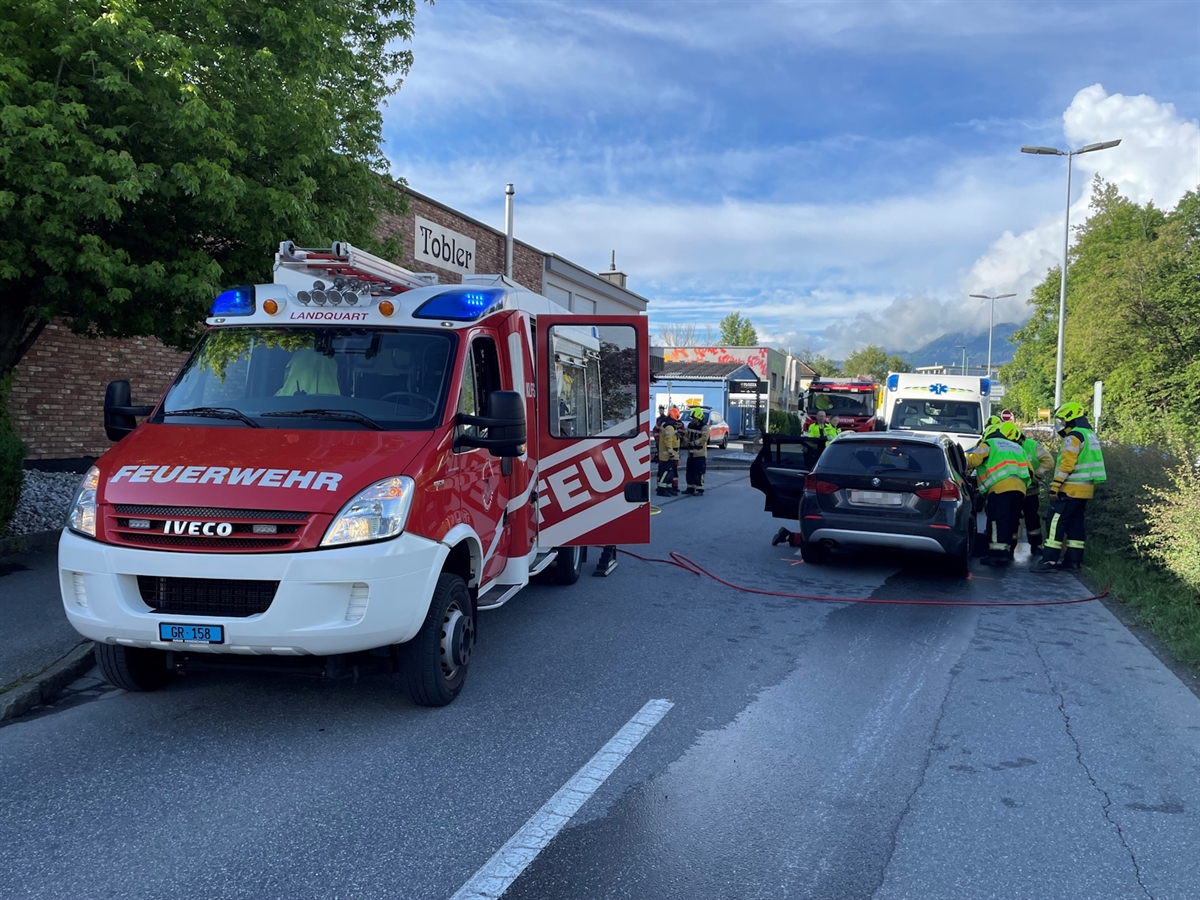 Ein Feuerwehrfahrzeug und eines der unfallbeteiligten Autos. Einsatzkräfte bei der Bergung der Mitfahrerin. Im Hintergrund leicht bewölkter Himmel.