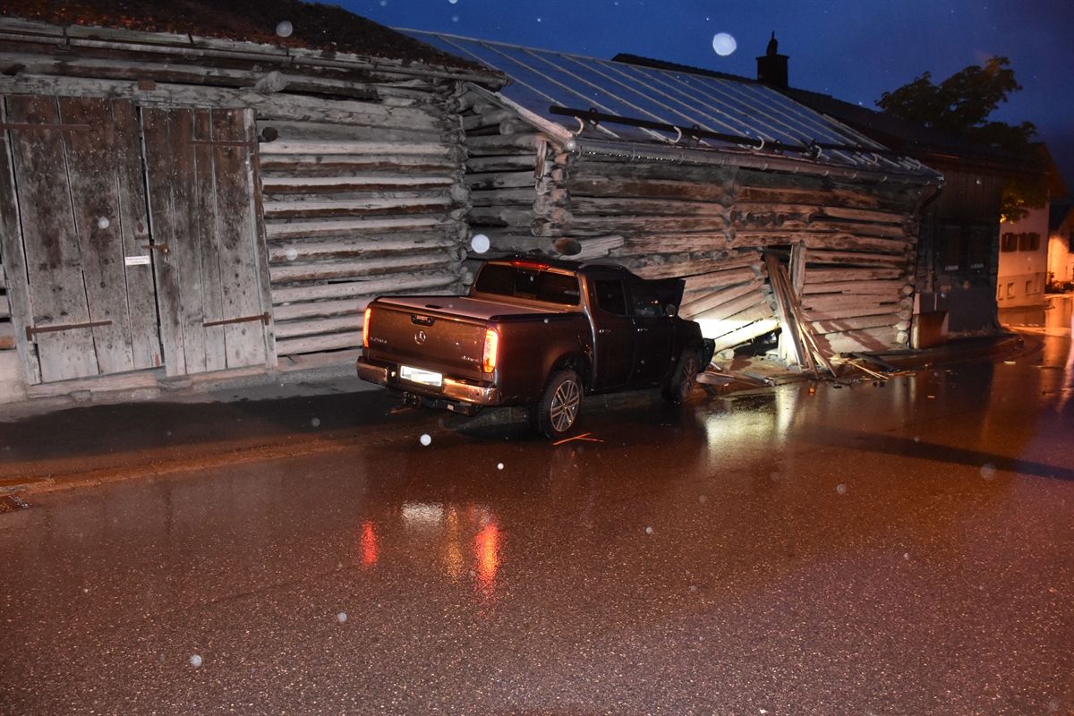Strassenverlauf innerorts in Tinizong im Bereich der Unfallstelle. In der Mitte des Bildes ist der massiv beschädigte Personenwagen sowie der Stallteil zu erkennen.