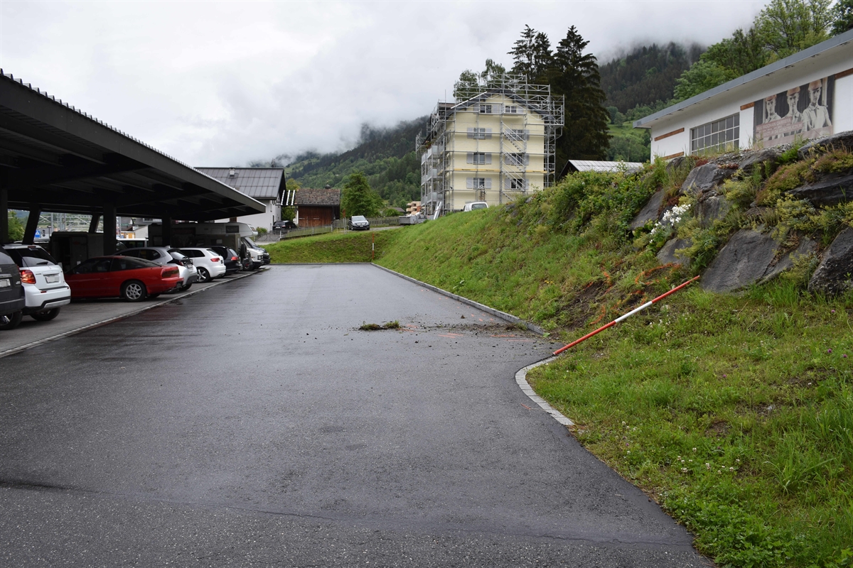 Kollisionsstelle mit der betroffenen Böschung auf der rechten Seite. Auf der linken Seite sind unter einem Unterstand Fahrzeuge abgestellt.