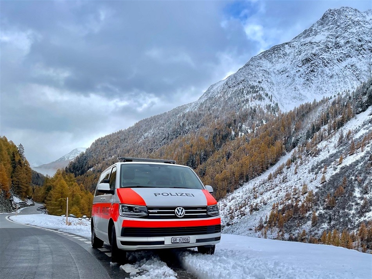 Ein Einsatzfahrzeug der Kantonspolizei Graubünden steht am Strassenrand im Schnee. Im Hintergrund winterliche Bergkulisse.