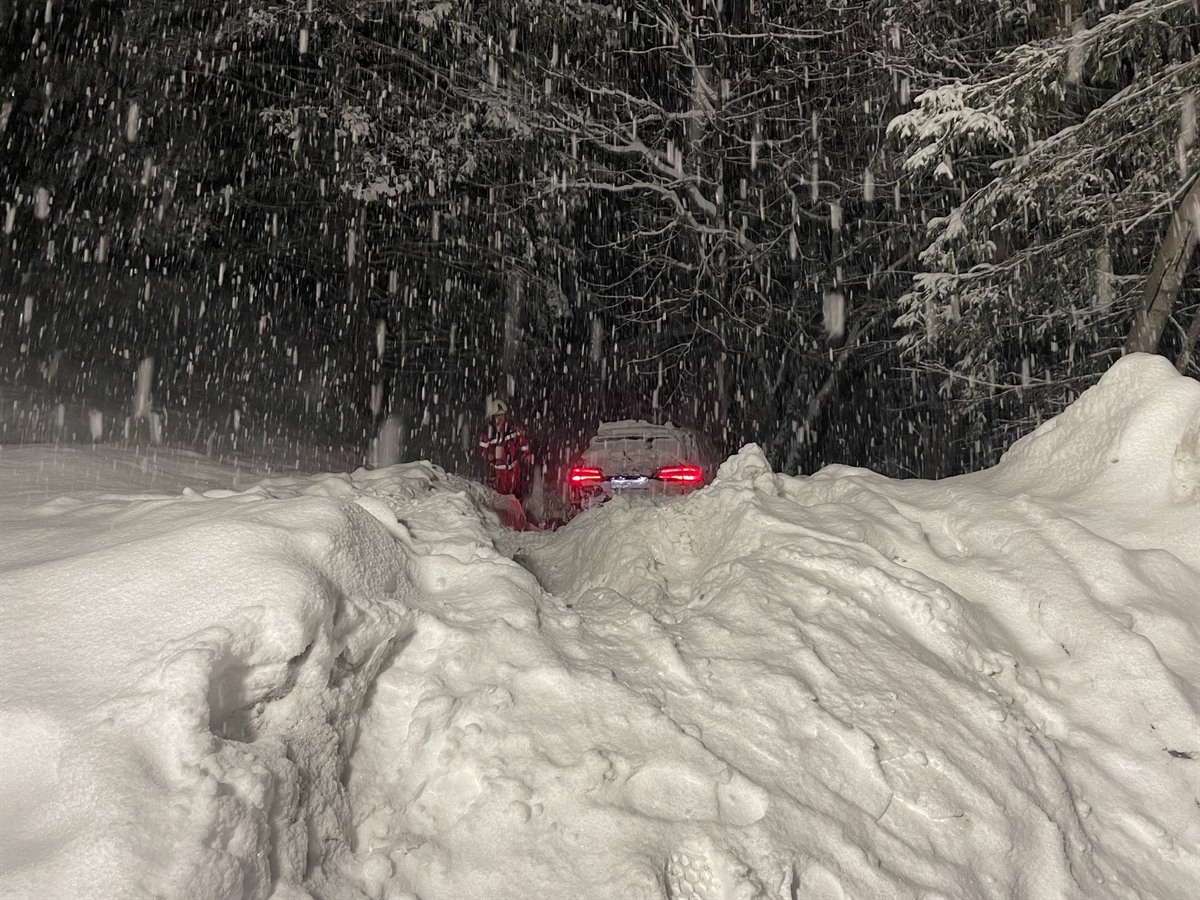 Tief im Schnee versunkenes Auto am Abhang mit Feuerwehrmann
