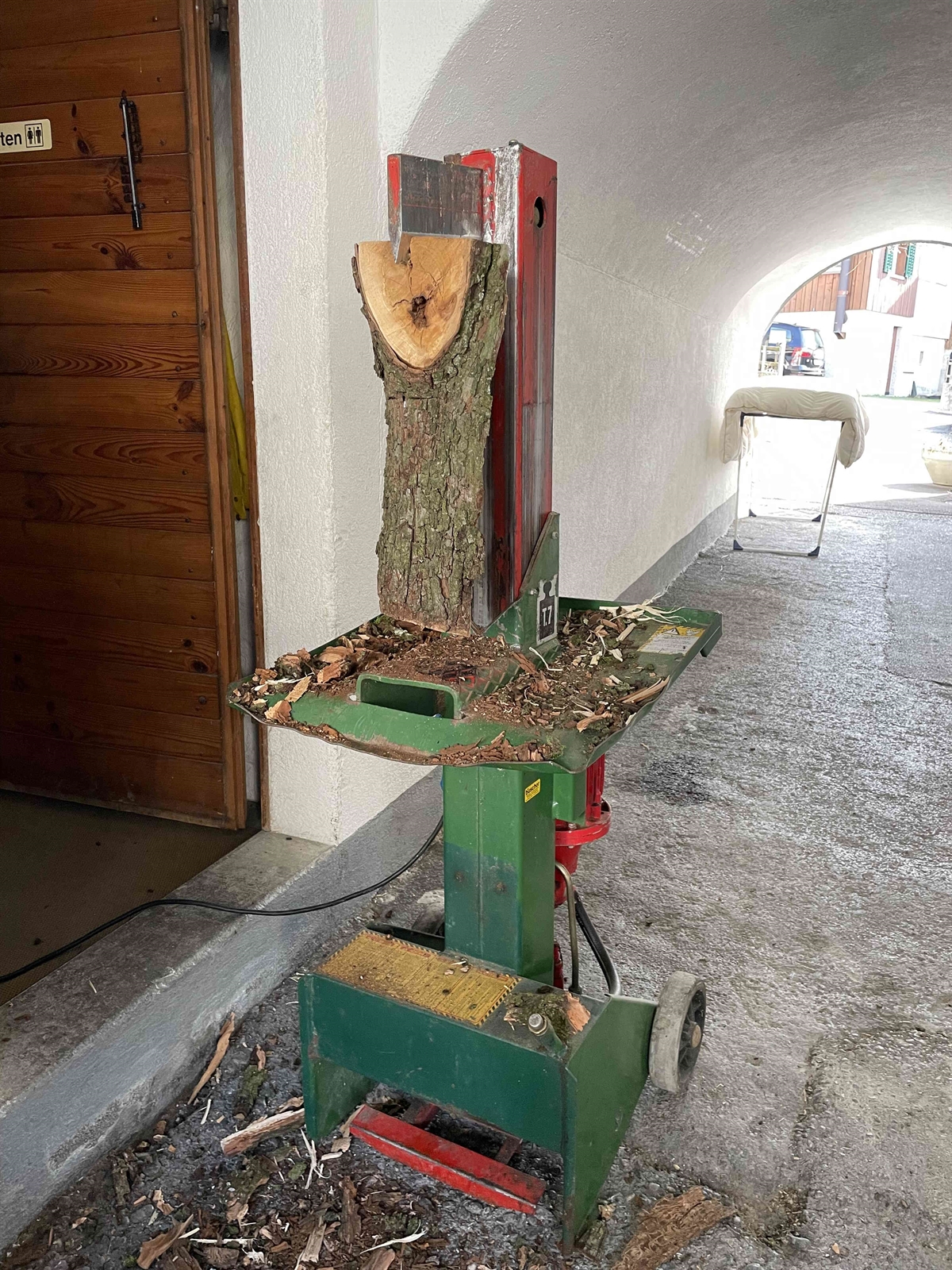 Übersichtsaufnahme der hydraulischen Holzspaltmaschine mit dem zum spalteten Holz auf der Maschine im Keil steckt.