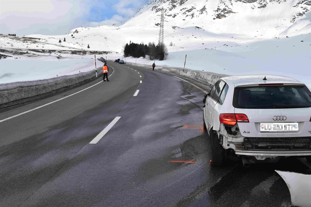 Im Vordergrund rechts steht der weisse beschädigte Personenwagen am rechten Strassenrand und ganz im Hintergrund steht der andere Unfallbeteiligte Personenwagen ebenfalls ganz am rechten Strassenrand. Am linken Strassenrand steht ein Polizist.