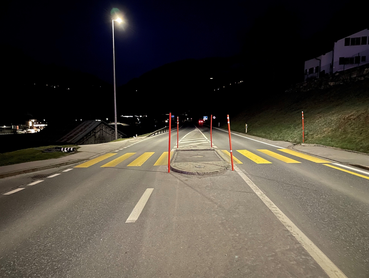 Aufnahme in der Dunkelheit. Die beleuchtete Mittelinsel mit Fussgängerstreifen. Am linken Strassenrand ein beschädigter Inselpfosten.