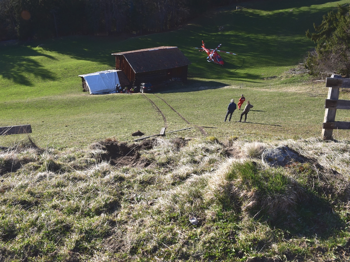 Blick vom Feldweg über die abfallende Wiesenböschung zur Endlage am Stall hinunter. Rechts davon der Rega-Helikopter.