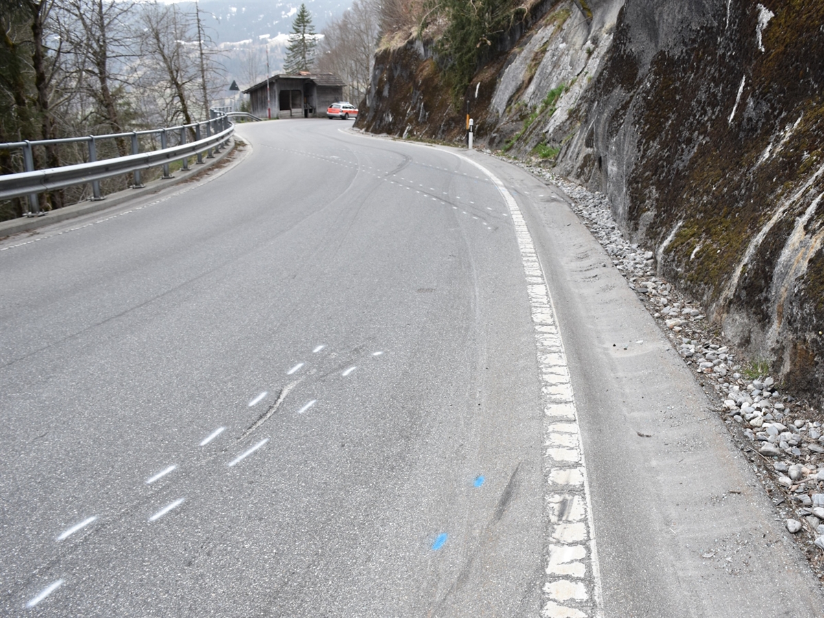 Kurviger Strassenverlauf. Eingezeichnete Unfallspuren. Im Hintergrund ein Polizeiauto.