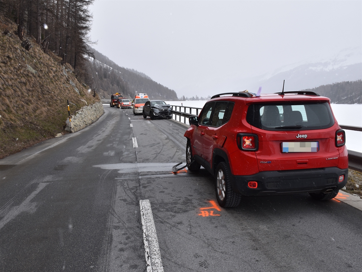 Im Vordergrund ein unfallbeteiligtes Auto von hinten. Etwas entfernt das andere beteiligte Auto mit starkem Frontschaden. Dahinter ein Rettungswagen, ein Polizeiauto und ein Abschleppfahrzeug.