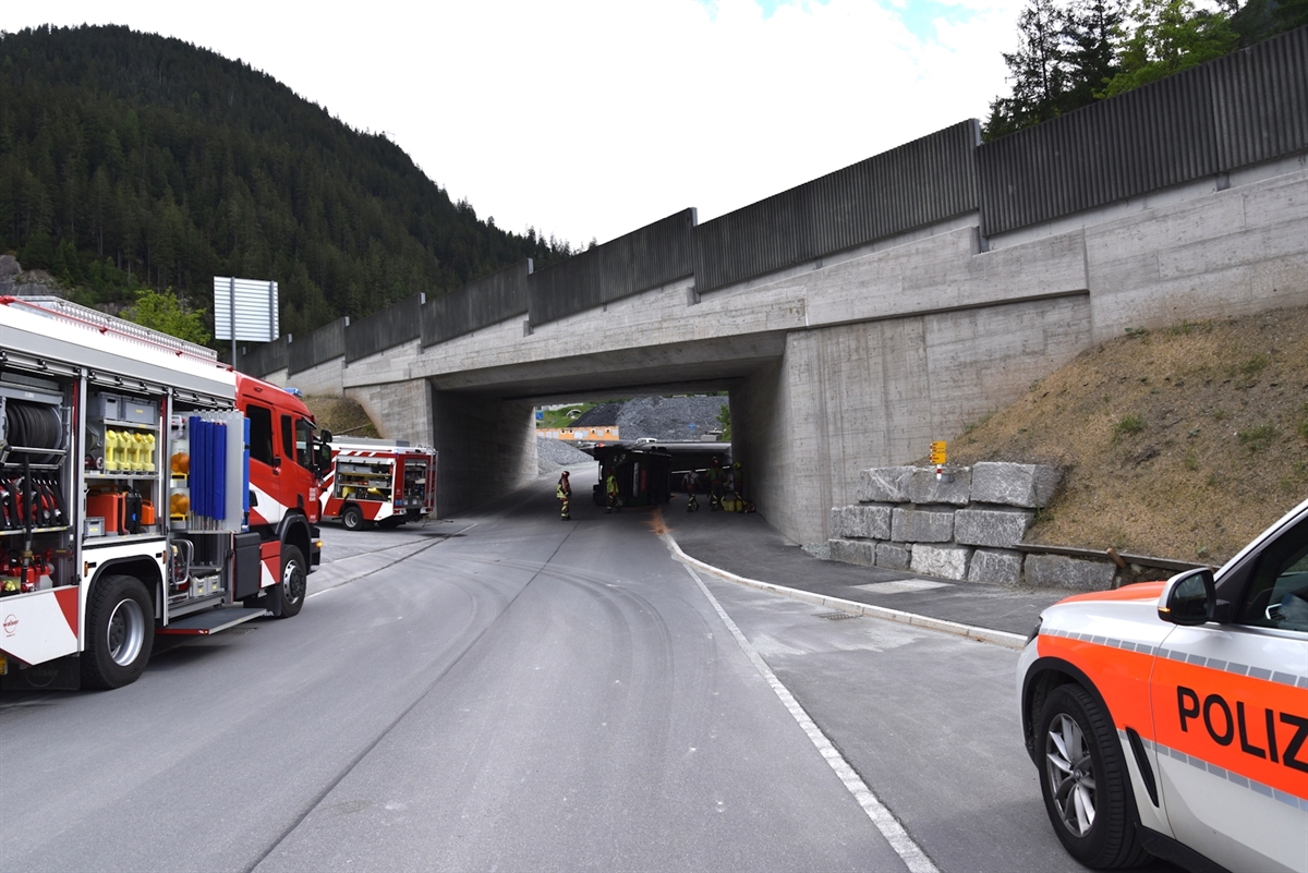 Von vorne das umgekippte Sattelmotorfahrzeug – davor Einsatzkräfte - in der Unterführung. Links zwei Feuerwehrautos, rechts ein Polizeiauto.  
