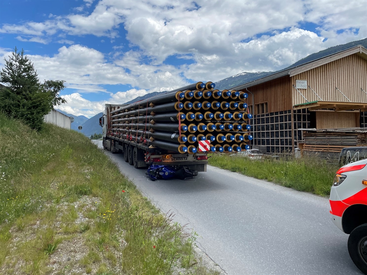 Das Sattelmotorfahrzeug mit der nach hinten überragenden Ladung steht auf der Auffahrt zur Oberalpstrasse. Unter dem Heck des Sattelaufliegers liegt das Motorrad. Am rechten Bildrand ragt die Front des Rettungswagens ins Bild hinein.