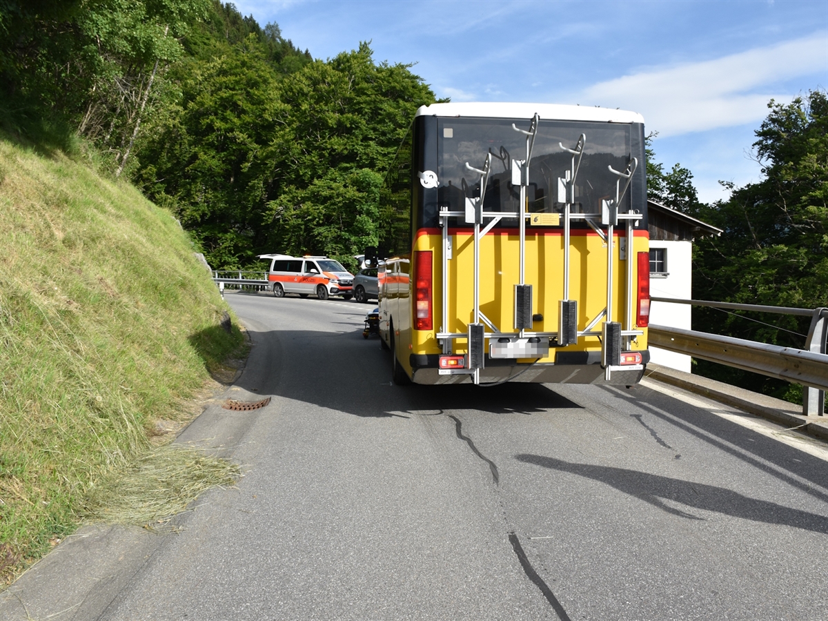 Ein Postauto von hinten. Im Hintergrund die Kurve und ein Polizeiauto. 