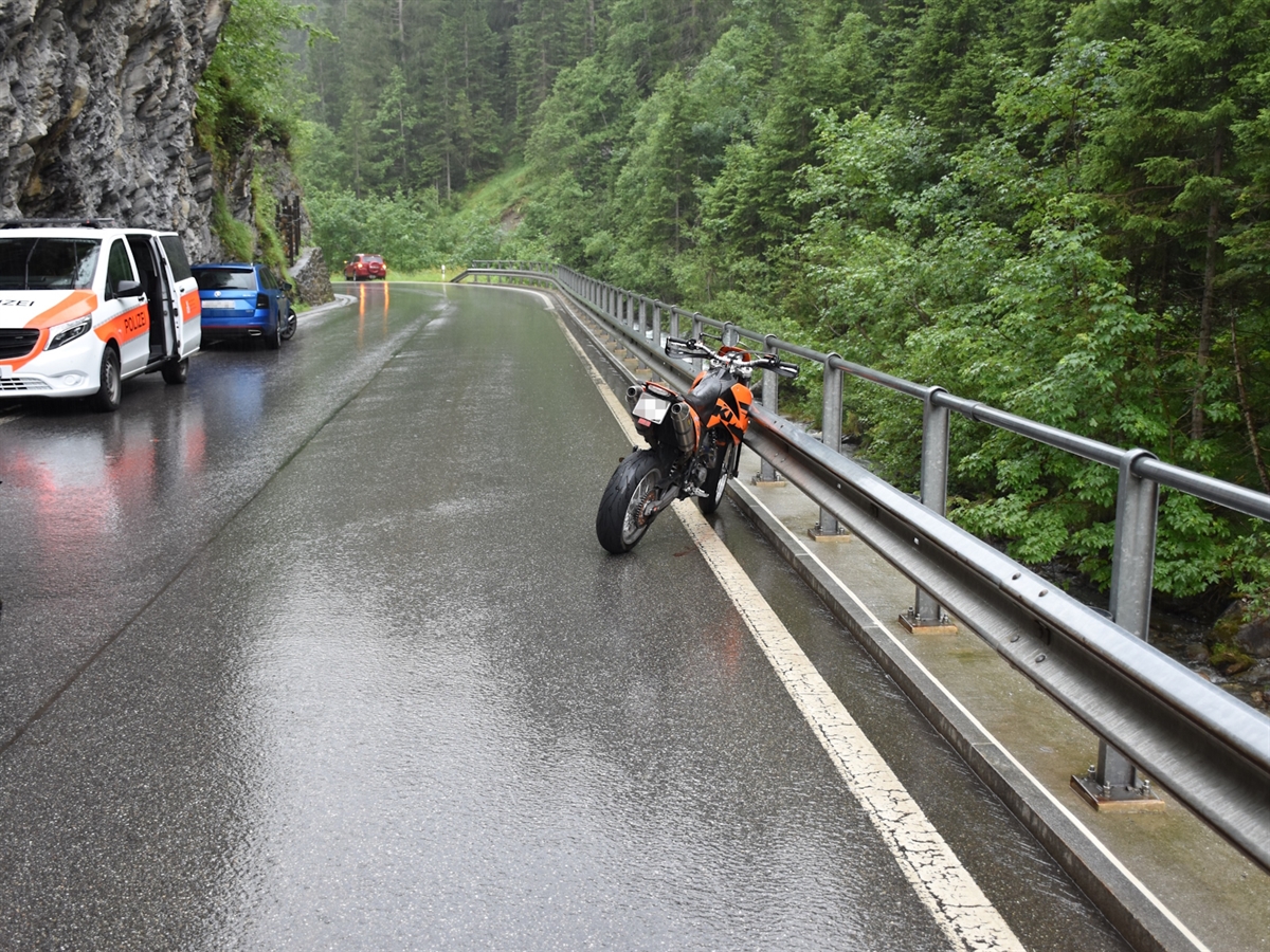 Rechts an einer Leitplanke lehnt das Unfallmotorrad. Links davon am Strassenrand ein Polizeiauto. Im Hintergrund die erwähnte Kurve. 