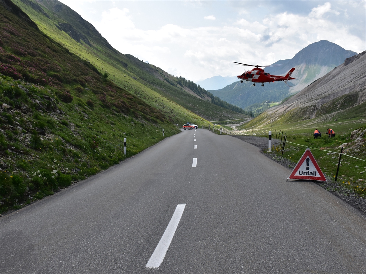 Der Rega-Helikopter hebt zum Überflug ins Spital auf der Unfallstelle ab. Zwei Polizisten schützen sich vom Downwash