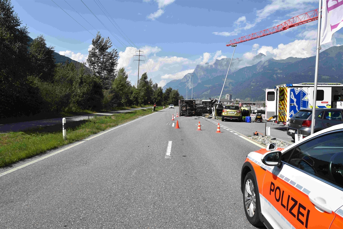 Gerades Strassenstück, im Vordergrund rechts ist das Polizeiauto und im Hintergrund der auf der linken Seite liegende Lieferwagen, Ansicht Unterboden und rechts davon der unfallbeteiligte Personenwagen auf dem Firmenareal. 