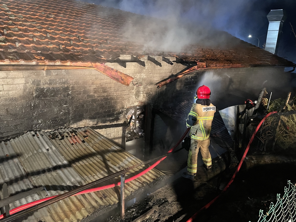Ein Feuerwehrmann bei  Löscharbeiten. Aus dem Gebäude steigt Rauch auf.