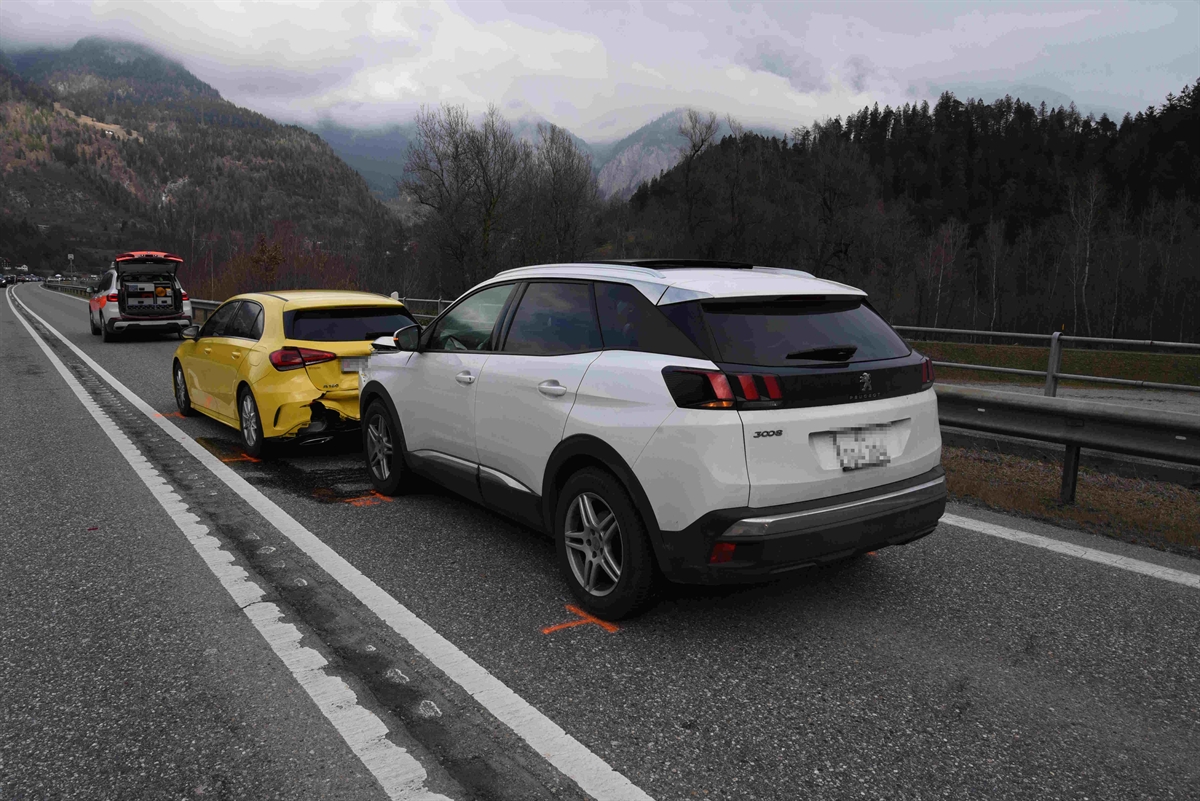 Nahaufnahme der beiden Personenwagen, vorne ein gelber und hinten ein weisser, stehen auf der Fahrbahn. Im Hintergrund steht das Polizeiauto mit geöffneter Heckklappe.