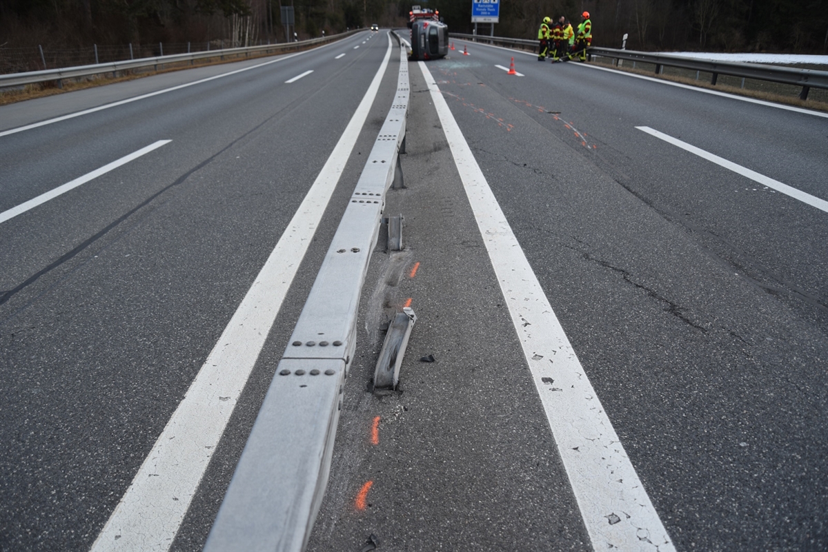Fahrzeug liegt total beschädigt auf der rechten Fahrzeugseite, rechts davon sind Einsatzkräfte der Feuerwehr 