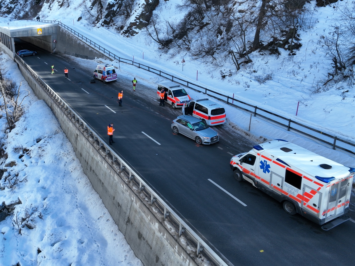 Die Örtlichkeit Charnadüra vor der Galerie in Richtung Celerina gesehen. Auf der Engadinerstrasse stehen die beiden Unfallautos sowie zwei Rettungswagen und zwei Patrouillenfahrzeuge. Polizisten und Rettungssanitäter bewegen sich auf der Unfallstelle.