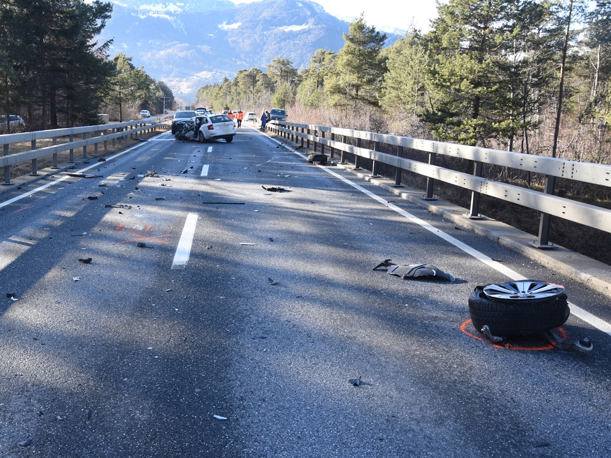 Die Unfallstelle mit verschiedenen Fahrzeugteile auf der Fahrbahn. Im Hintergrund zwei Unfallfahrzeuge. Polizisten begutachten die Unfallstelle.