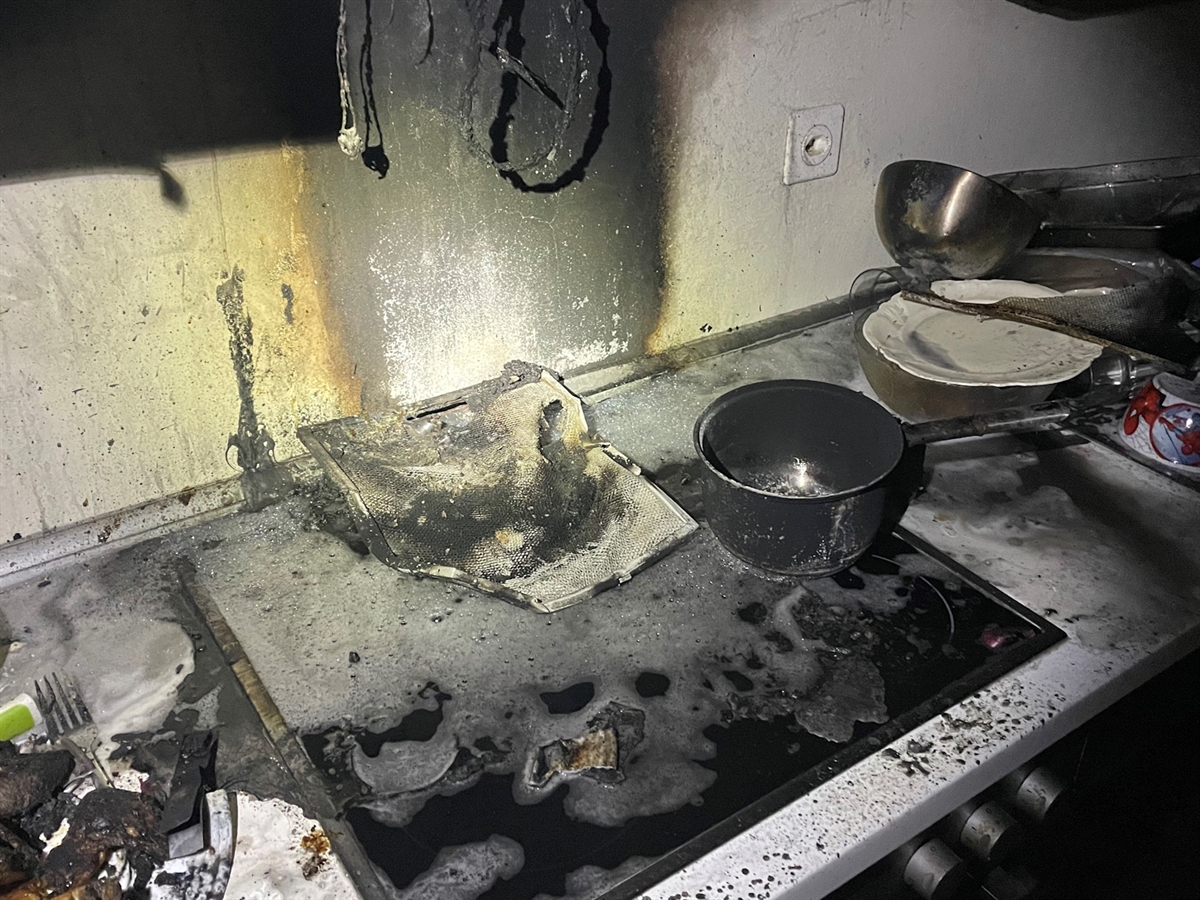 Auf dem mit Rus verschmutzten Küchenherd steht eine verkohlte Pfanne. Angesengte Elektrokabel hängen vom Oberschrank herunter.