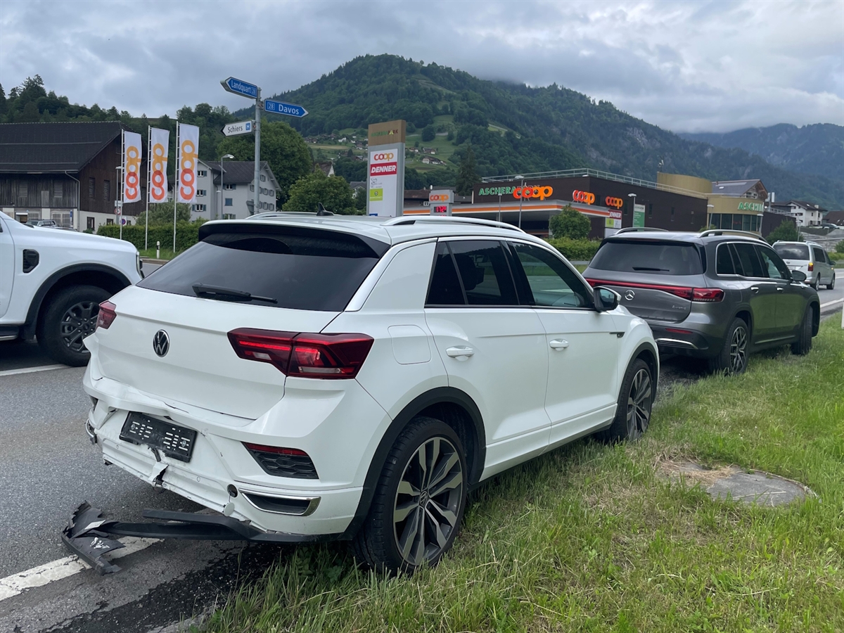 Aufnahme von schräg hinten auf die beiden vorderen Autos. Sie stehen halb auf der Strasse, halb in einer Wiese.