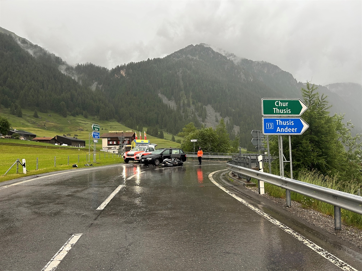 Die Italienische Strasse beim Anschluss Sufers. Vor dem Unfallauto liegt das Motorrad auf der Fahrbahn. Hinter dem Auto steht ein Patrouillenwagen und auf der Fahrbahn begutachtet ein Polizist die Unfallsituation