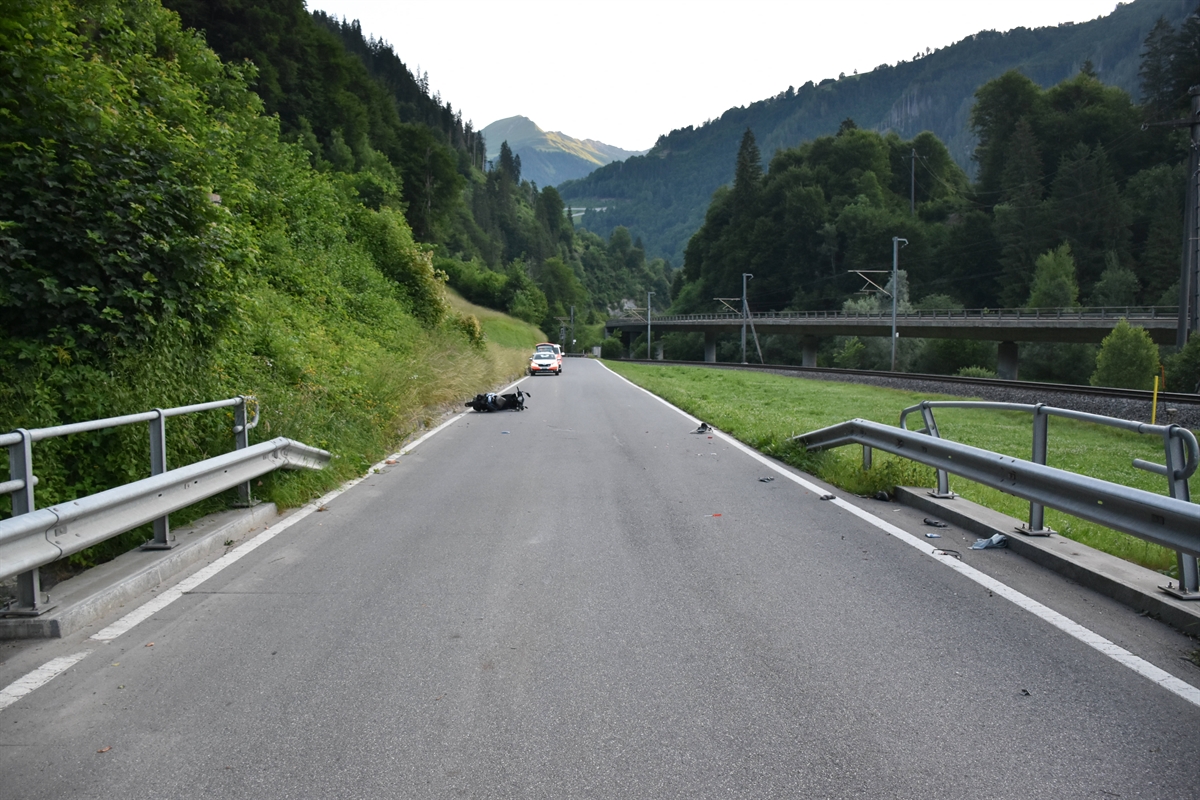 Strassenverlauf der Unfallstelle bei der Bachüberführung in Pragg-Jenaz. Auf der linken Strassenseite im Hintergrund die Endlage des beschädigten Motorrades. Weiter hinten ist noch ein Patrouillenfahrzeug zu erkennen.