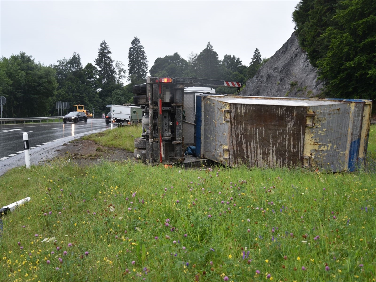 Der Lastwagen liegt auf der rechten Seite im Wiesland. Im Hintergrund die Oberalpstrasse mit Fahrzeugverkehr