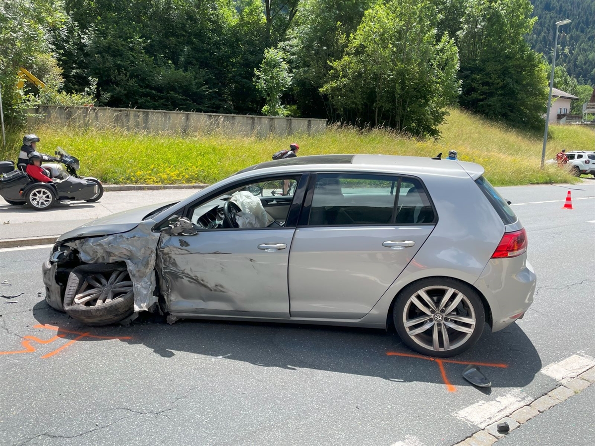 Das vorne links beschädigte Auto steht Quer auf der Fahrbahn. Motorräder fahren an dem Auto vorbei.