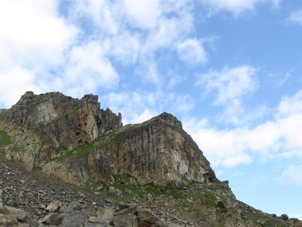 Sicht von unten auf den Nordostgrat des Chilbiritzenspitzes. Er grenzt sich von leicht bewölktem Himmel ab.