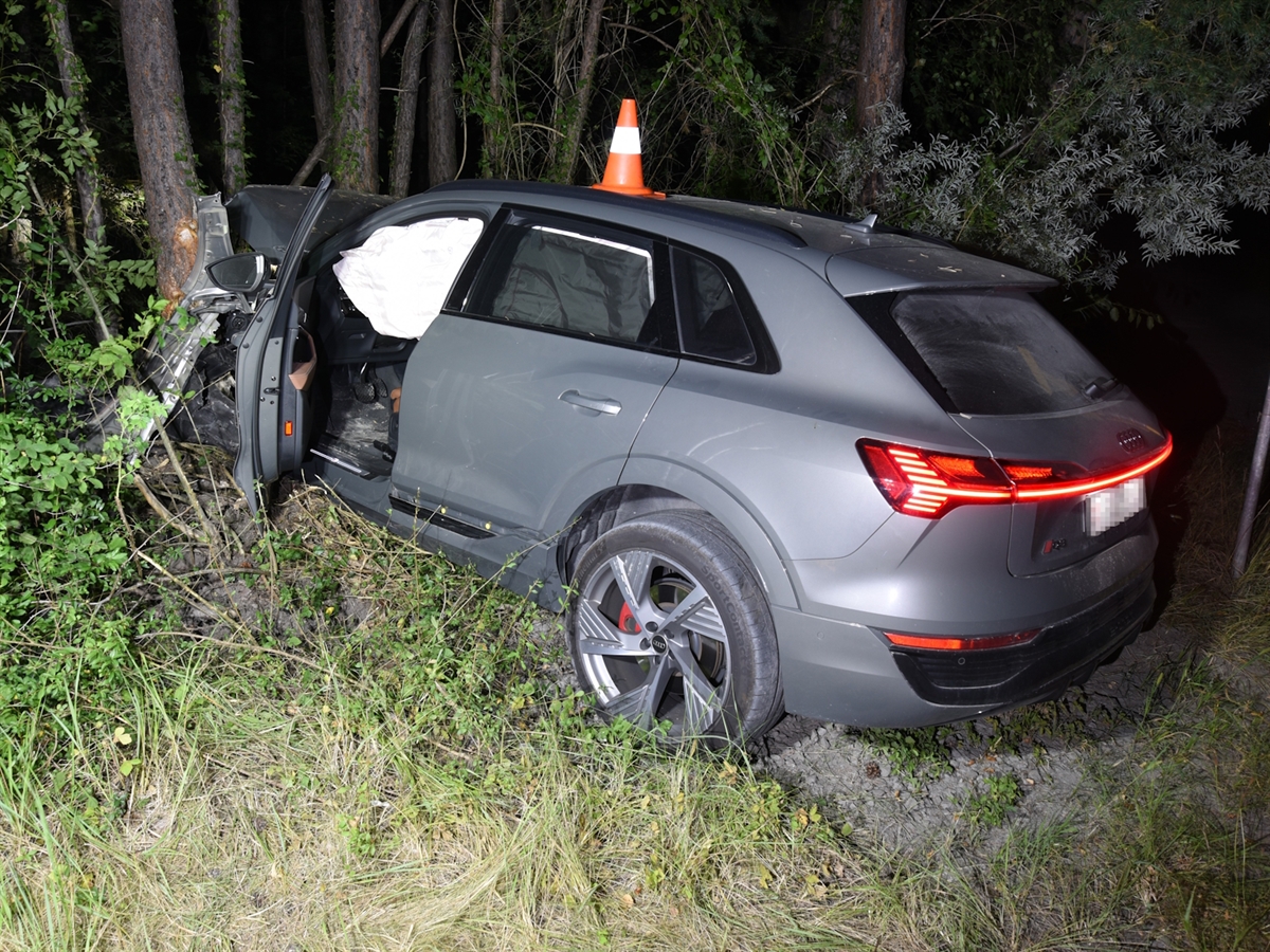 Nachtaufnahme des Unfallautos. Die Front ist in den Bäumen verkeilt. Auf dem Autodach steht zur Kennzeichnung der Endlage ein Leitkegel der Polizei.