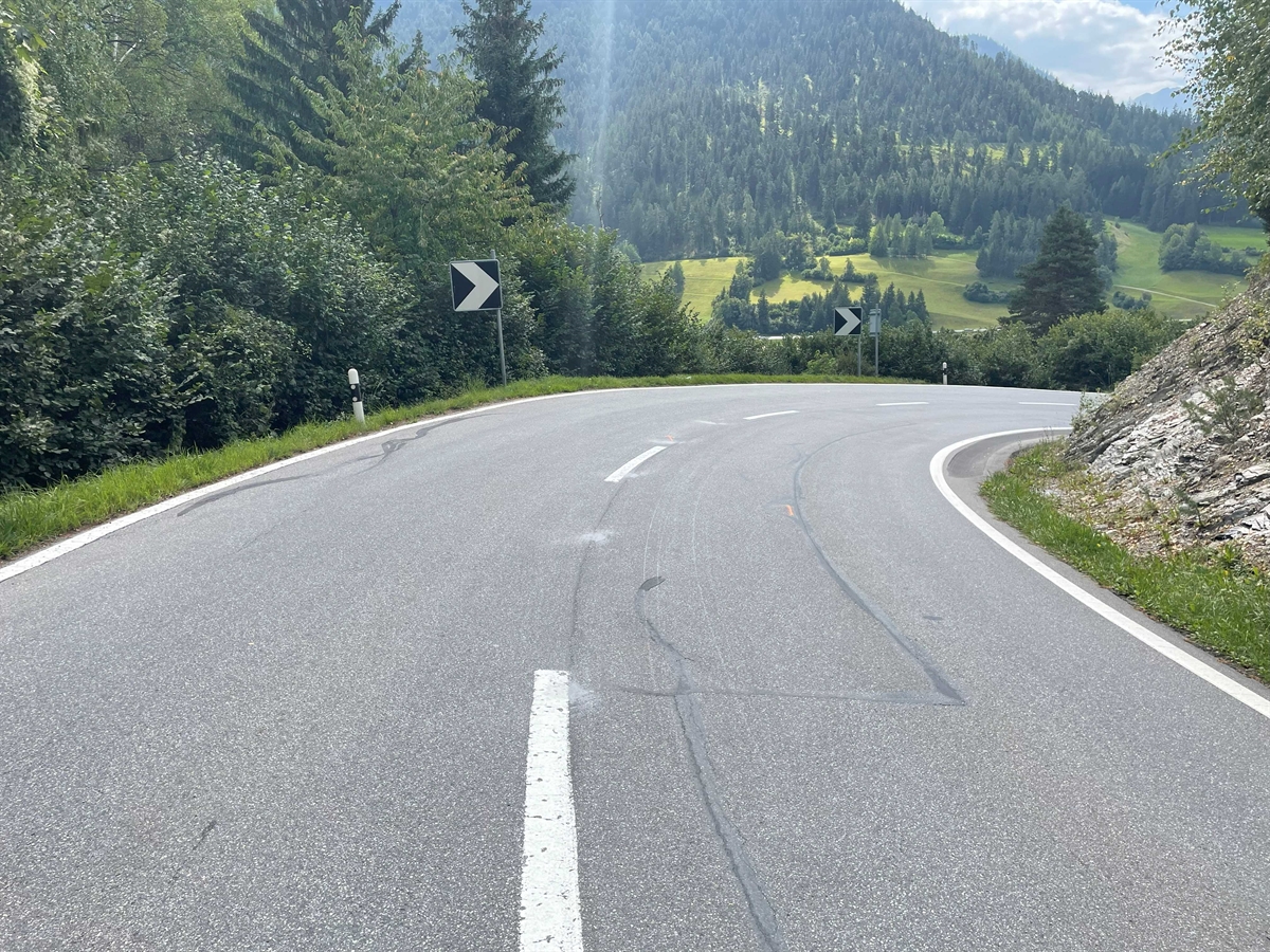 Abfallende Strasse mit Kurve. Auf Fahrbahn aufgetragene Unfallmarkierungen.